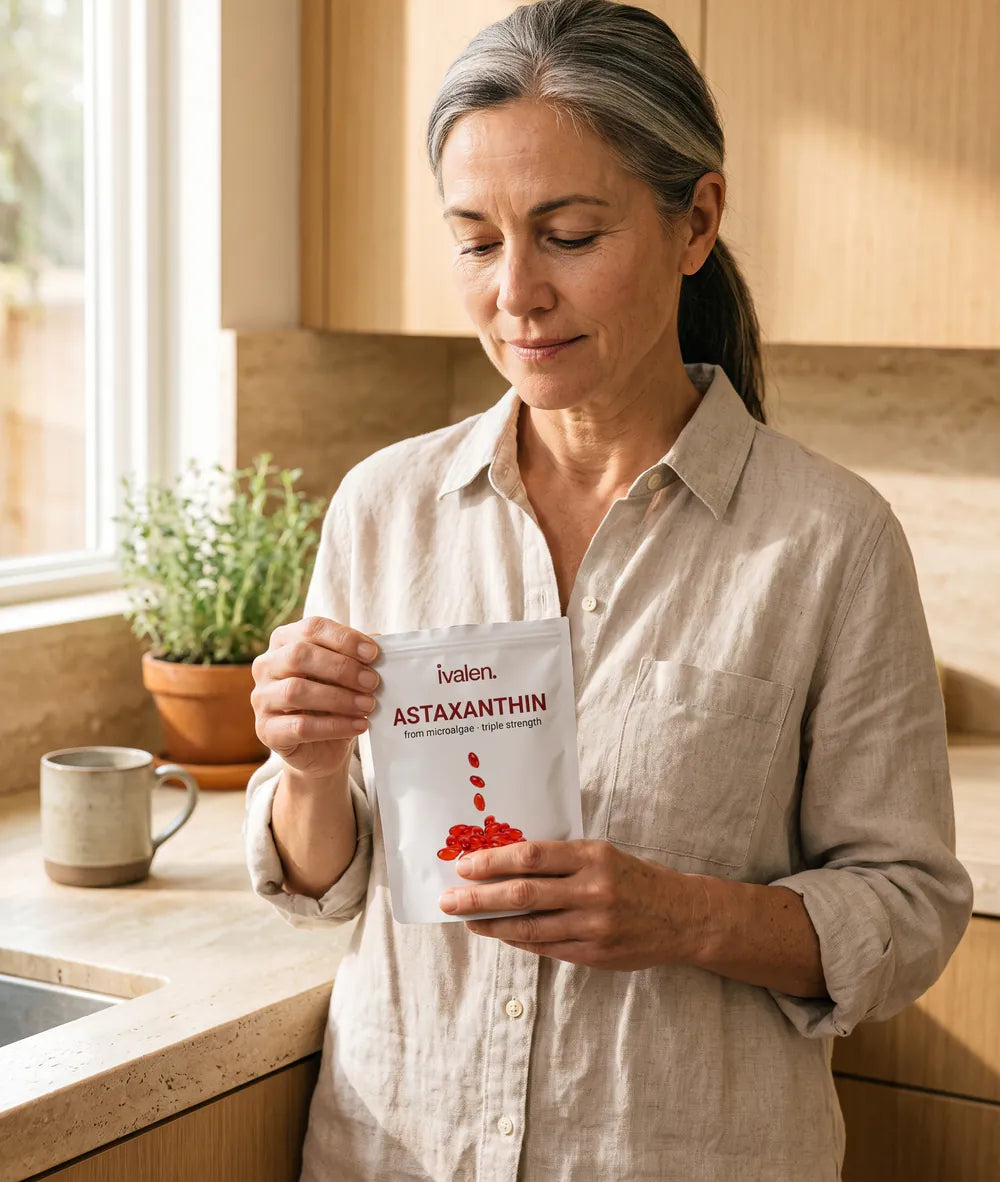 A woman in her fifties holding a pouch of Ivalen Astaxanthin at her kitchen counter in morning light